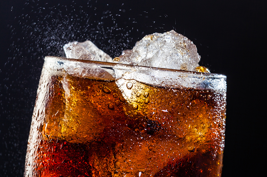 Glass of sparkling water with ice cubes and slice of lime A glass with cola and ice cubes