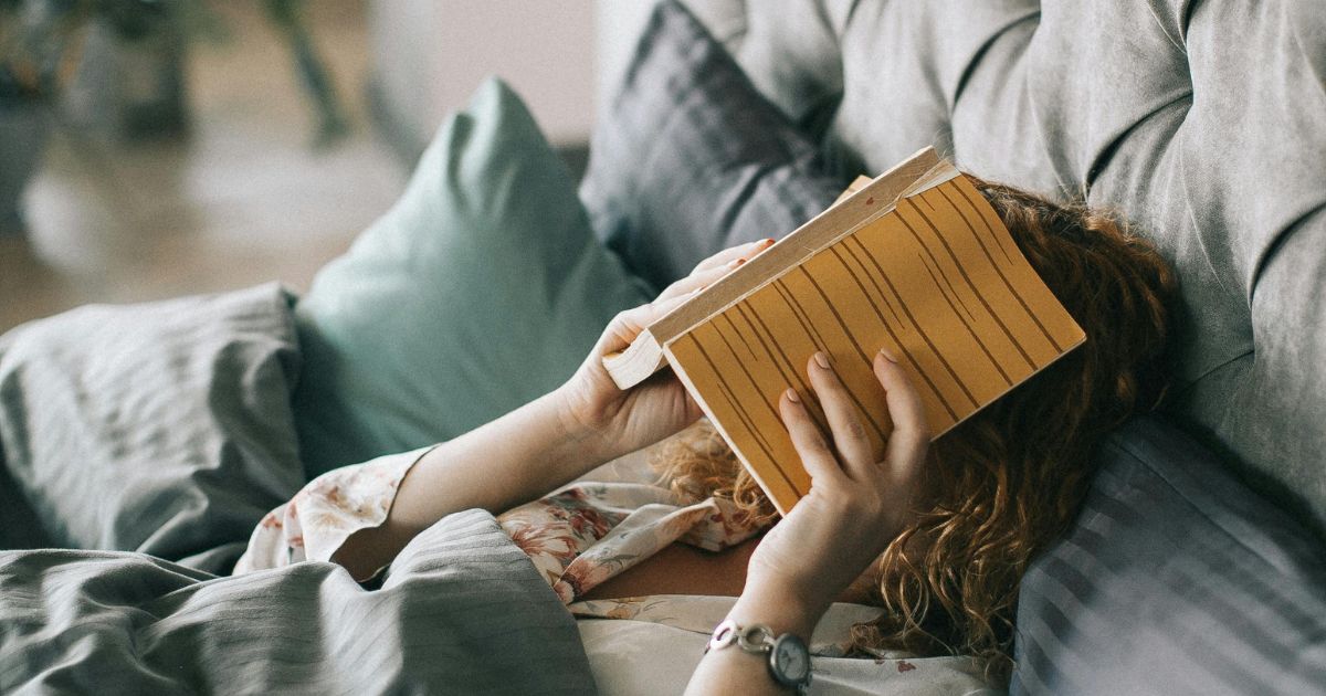 person lying on bed and covering face with a book