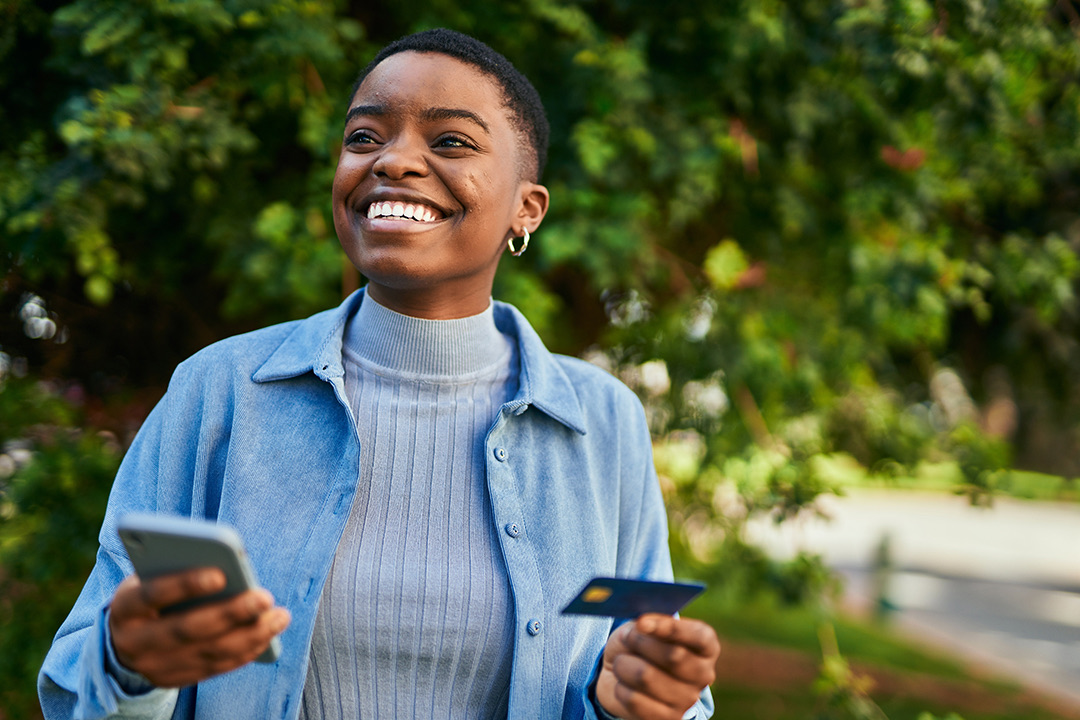 Young african american woman smiling happy holding smartphone and credit card at the city Young african american woman smiling happy holding smartphone and credit card at the city
