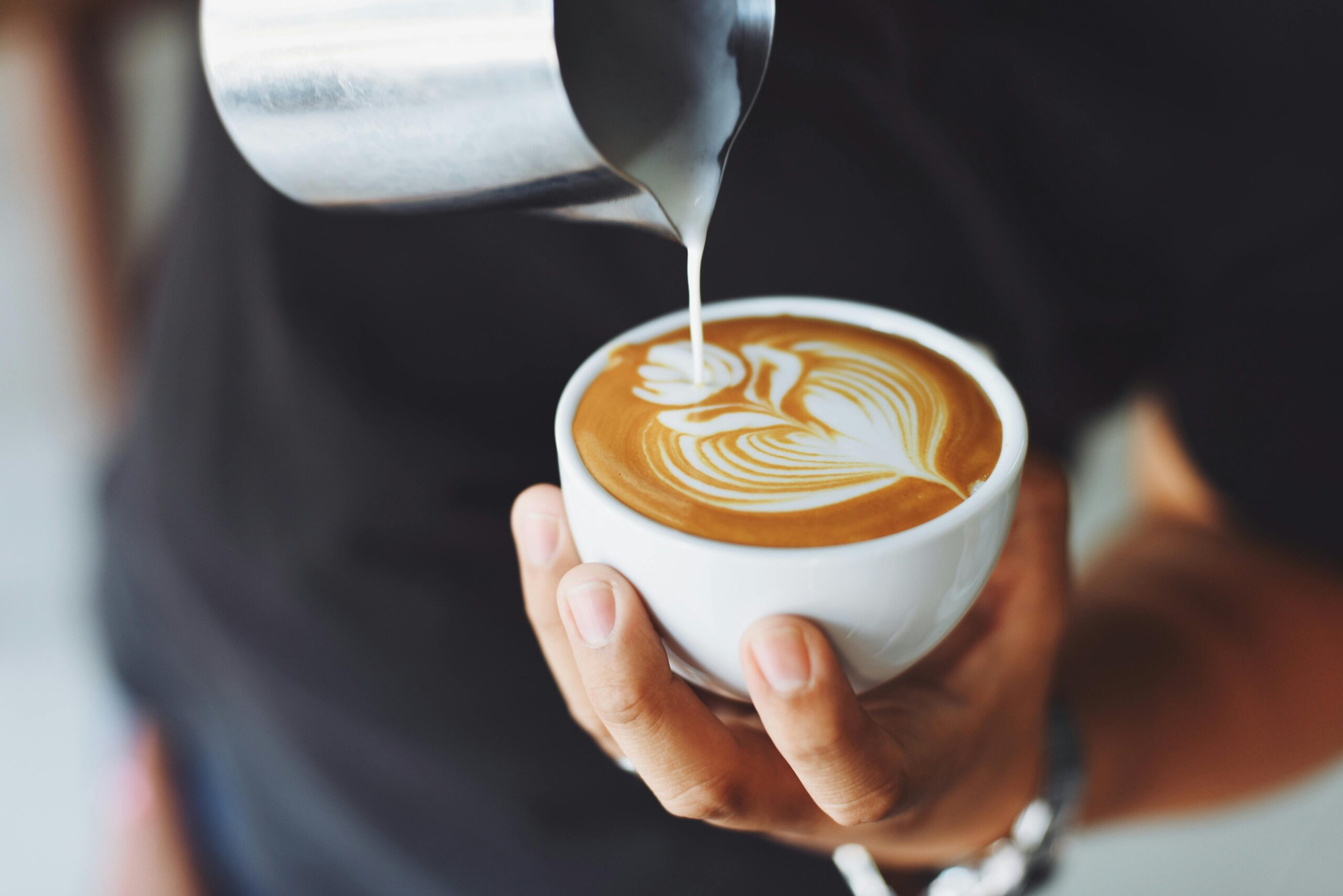 A person pouring frothed milk into a cup